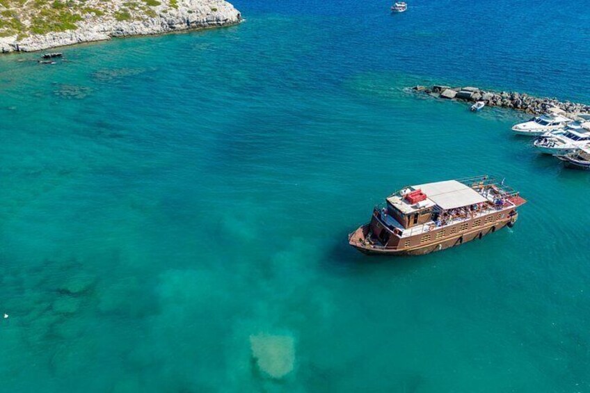 A boat on turquoise water near a rocky shore with other boats docked. 1