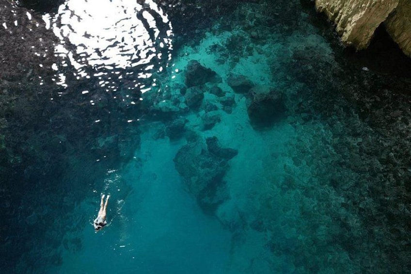 A person swimming in clear turquoise water with visible underwater rocks. 3
