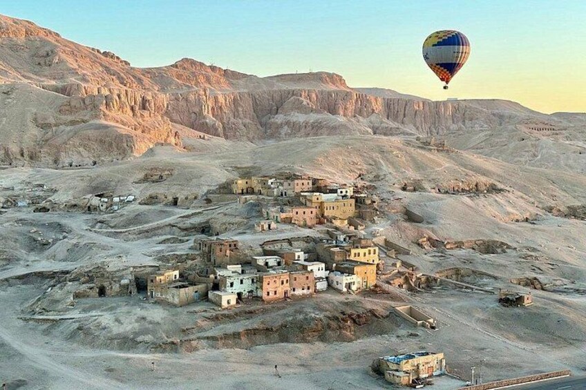 A desert landscape with a small settlement of buildings, a hot air balloon in the sky, and rocky hills in the background. 2