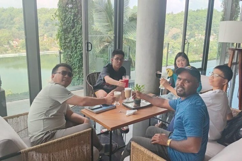 A group of people seated around a table with drinks, overlooking a lake and greenery. 5