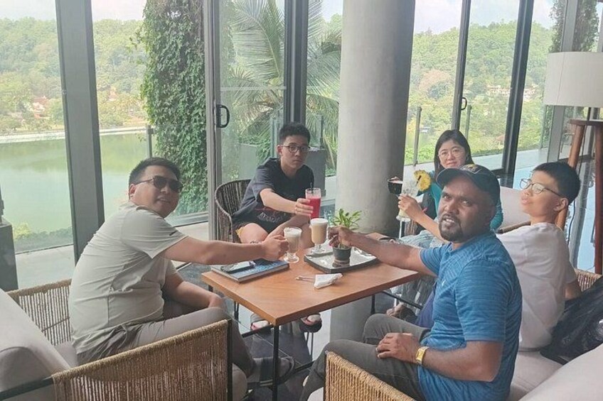 A group of people sitting around a table with drinks, overlooking a lake and greenery. 5