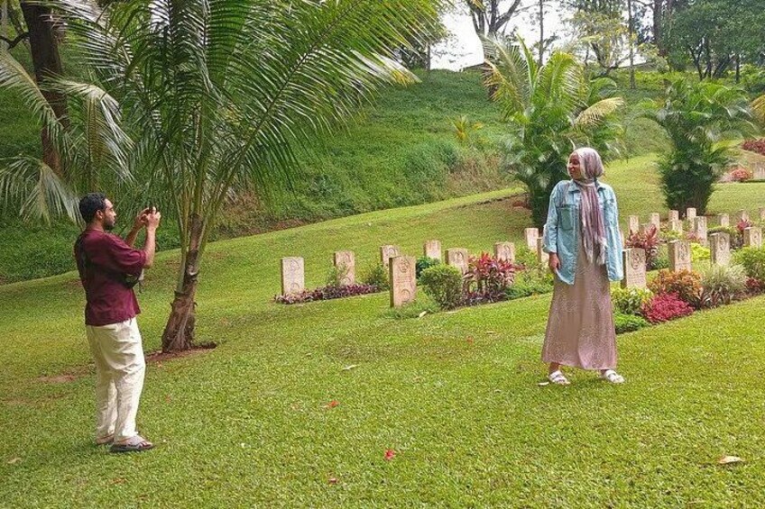 A person taking a photo of another person in a cemetery with tombstones and greenery. 1