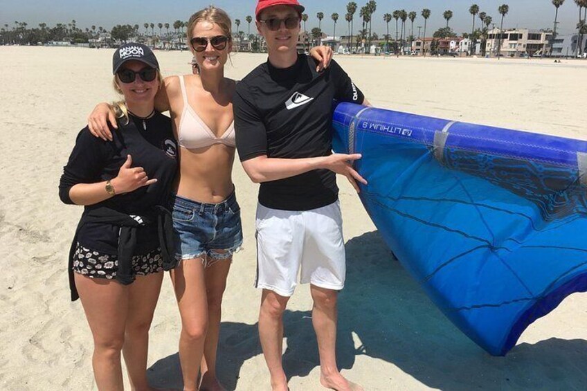 Three people on a beach with a blue inflatable surfboard. 2