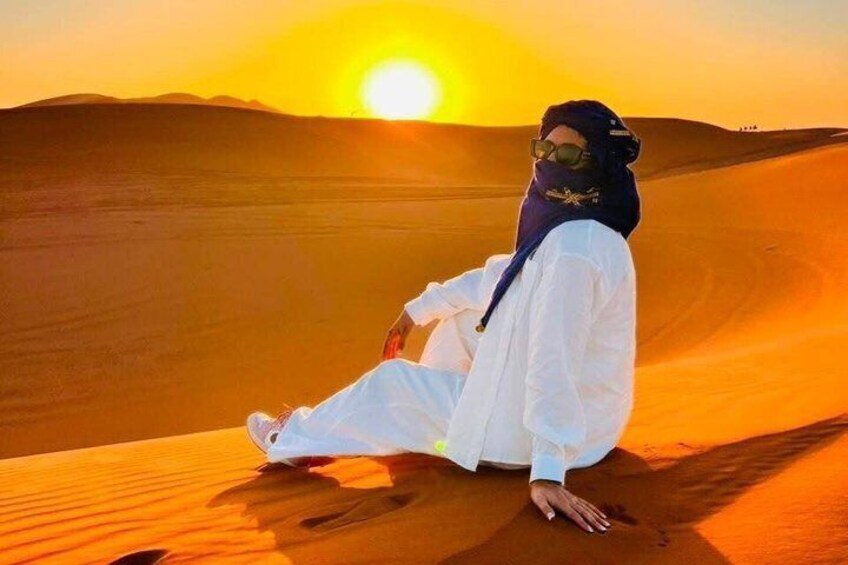 A person sitting on a sand dune with a sunset in the background. 2