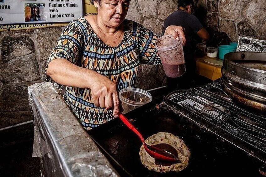 A person preparing a food item in a kitchen with a stone wall and a metal cooking surface. 4