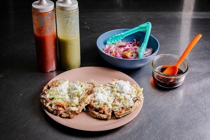 Two tacos on a plate, a bowl of pickled onions, and two condiment bottles. 3