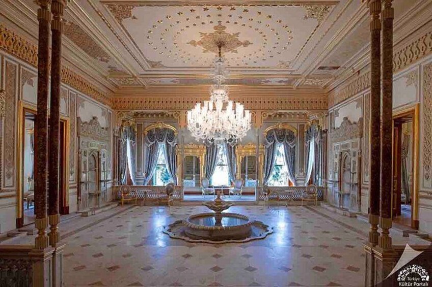 An opulent room with a grand chandelier, ornate columns, and a fountain. 3