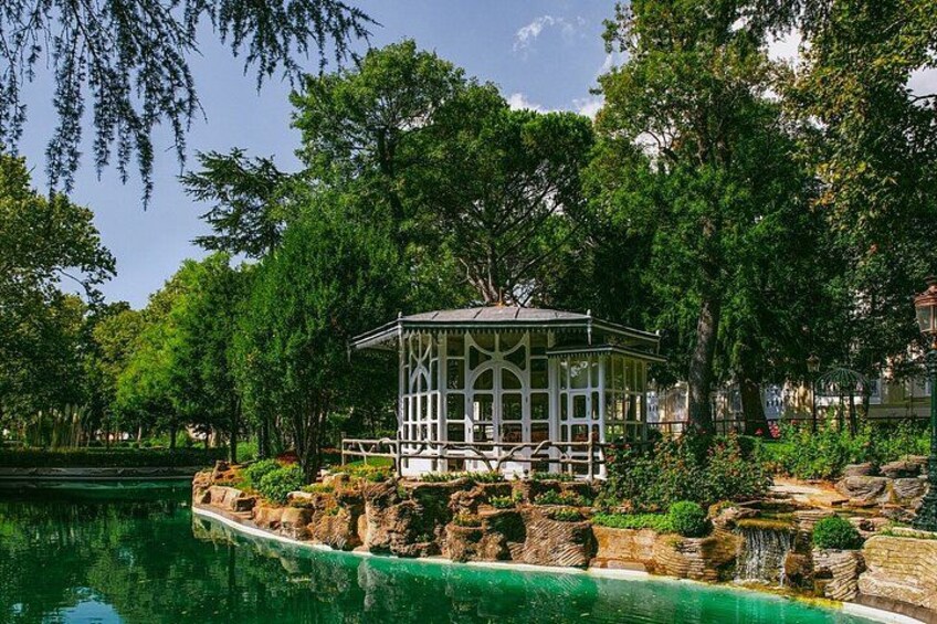 A gazebo by a calm lake surrounded by lush greenery. 5