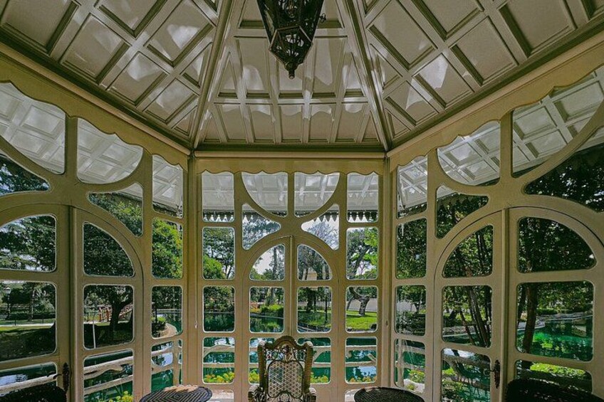 A conservatory with a glass roof, ornate white frame, and a central table. 2