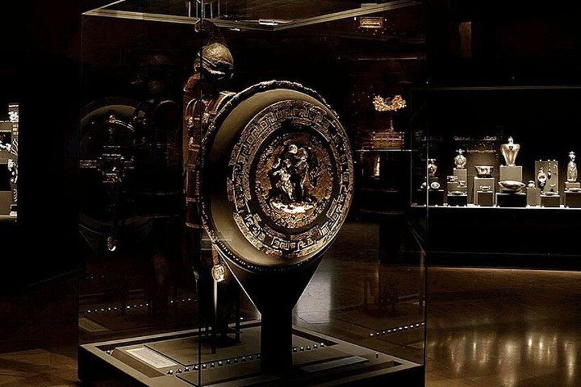 Une grande horloge richement décorée, ornée de motifs complexes et surmontée d’une figure centrale, exposée dans un musée, avec d’autres objets en arrière-plan. 3
