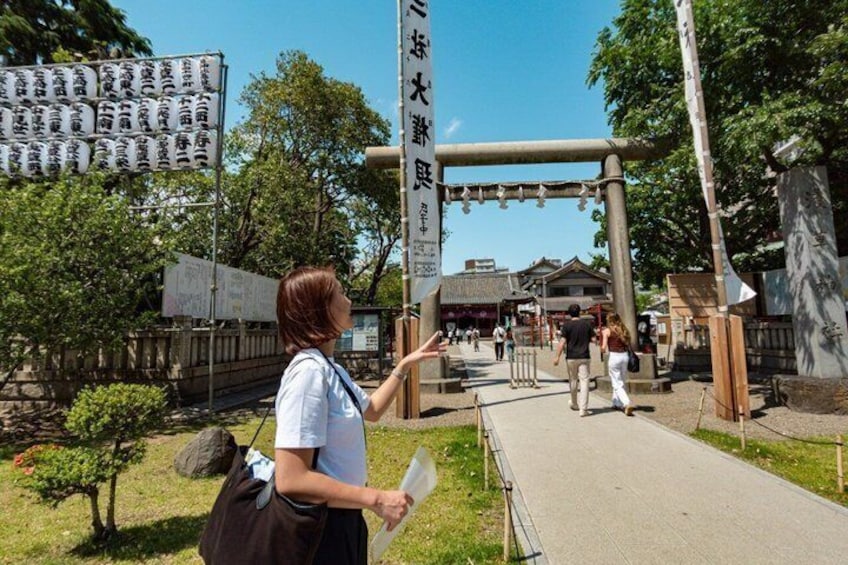 Eine Person zeigt auf ein Schild mit japanischen Schriftzeichen, ein traditionelles Tor und einen Weg, der zu einem Gebäude führt. 5