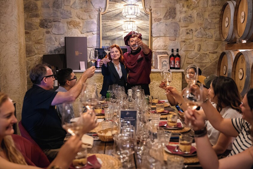 En gruppe mennesker skåler ved en vinsmagning, med vinglas og flasker på bordet. 2