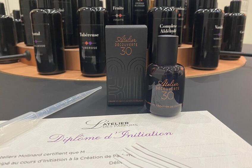 A display of L'Atelier de Découverte 30 products, including a box and a bottle, on a table with a diploma. 1