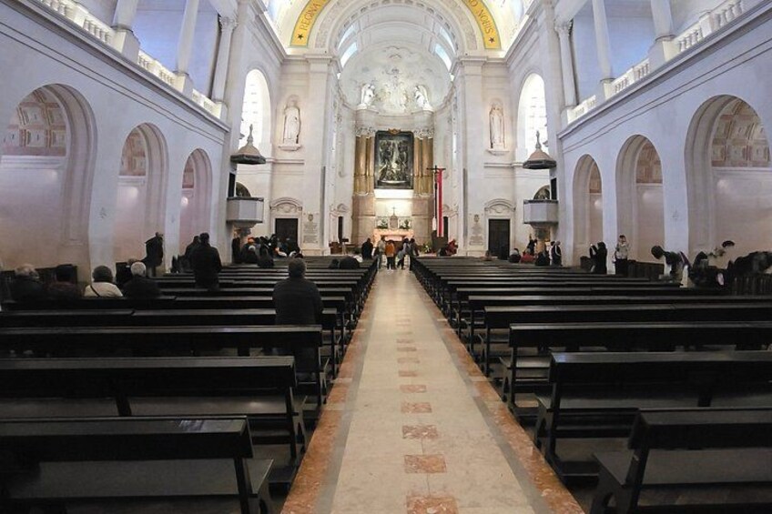 Interior de iglesia con hileras de bancas, un pasillo central y un techo alto con ventanales de arco. 4