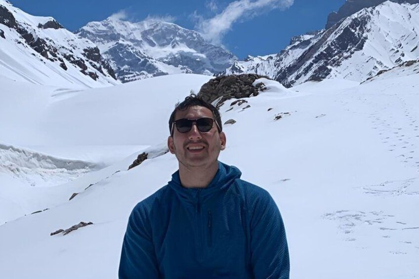 A person standing in a snowy mountainous area with rocky terrain and snow-covered peaks in the background. 1