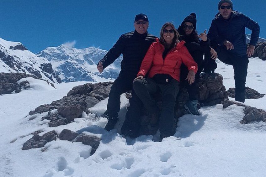 A group of people on a snowy mountain with rocky terrain and snow-covered peaks in the background. 4