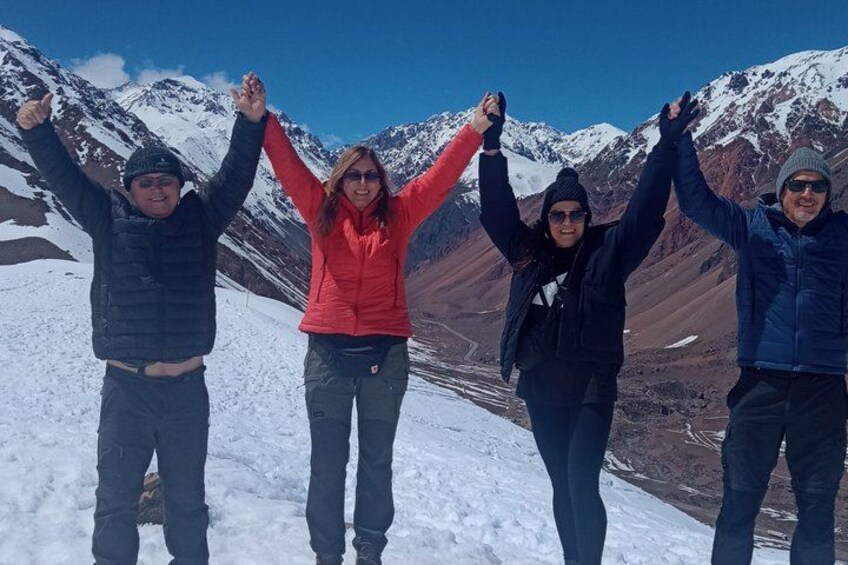 Four people standing on a snowy mountain with their arms raised, surrounded by snow-covered mountains. 2