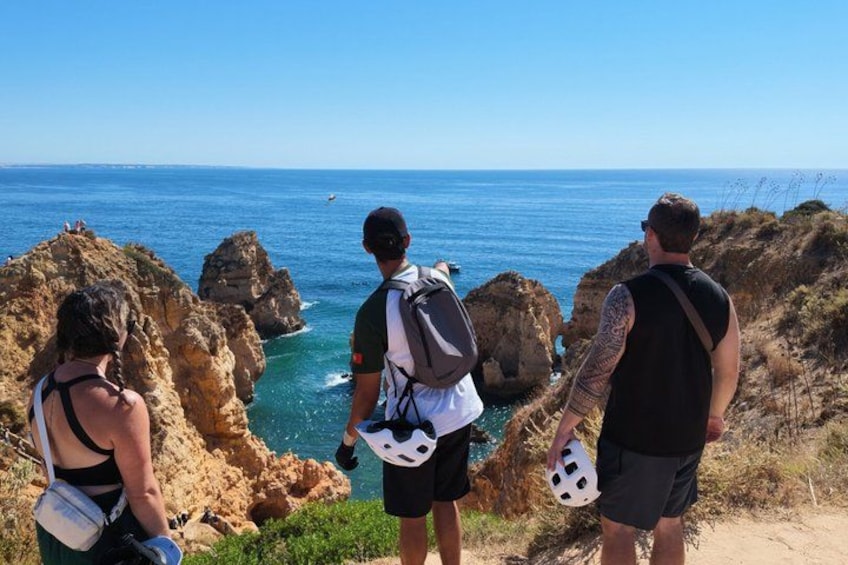Tres personas de pie en un acantilado rocoso con vista al océano. 4