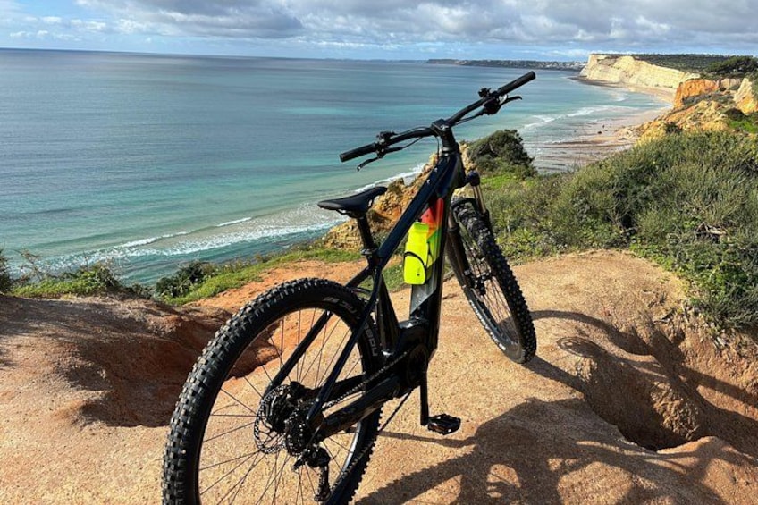 A mountain bike on a sandy cliff overlooking a beach with cliffs and ocean. 3