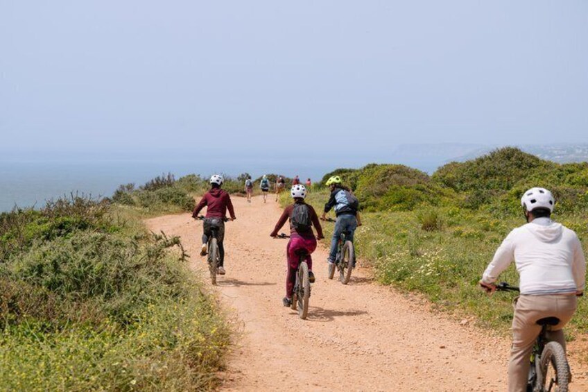 A group of cyclists on a dirt path with a coastal view. 1