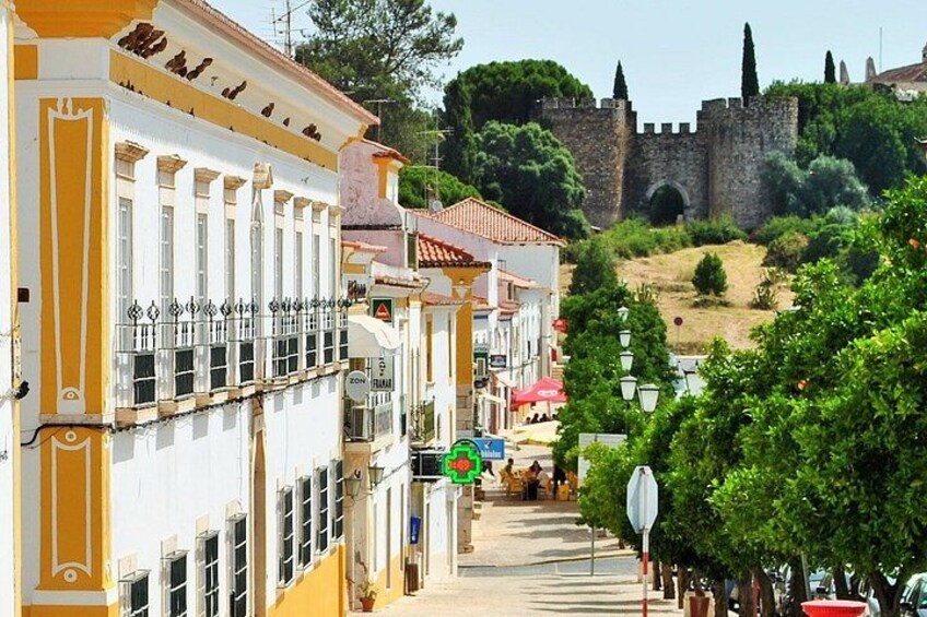 A street with buildings, a castle in the background, and a sign for a restaurant. 1