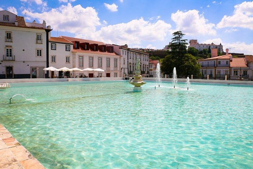 A clear pool with fountains, surrounded by buildings with red roofs and white walls. 2