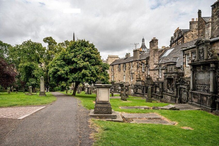 A cemetery with headstones, a pathway, and historic stone buildings. 5
