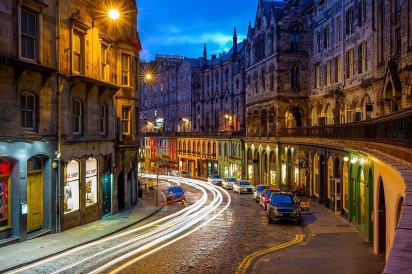 A nighttime street with historic buildings, a wet cobblestone road, and cars. 3