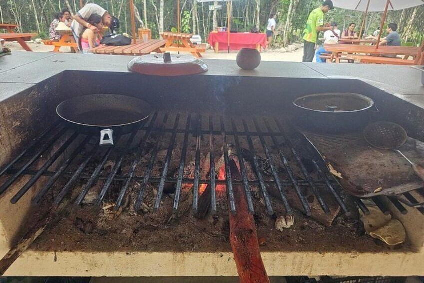 A barbecue grill with a pan and a pot, surrounded by wooden benches and tables. 3