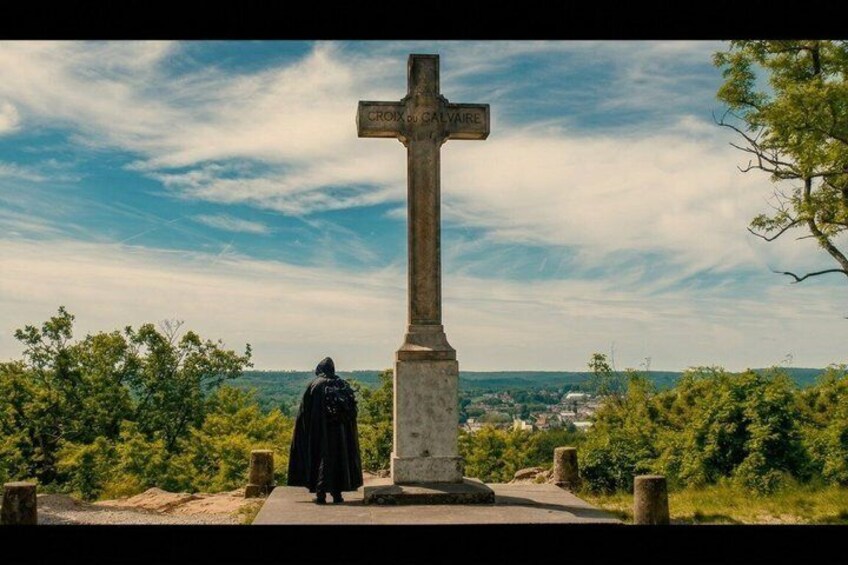 A cross with 'CROIX du CALVAIRE' inscribed, a person in black, and a landscape with trees and a distant town. 2