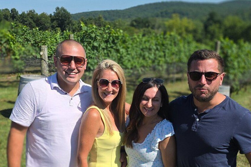 A group of people standing outdoors with a vineyard in the background. 2