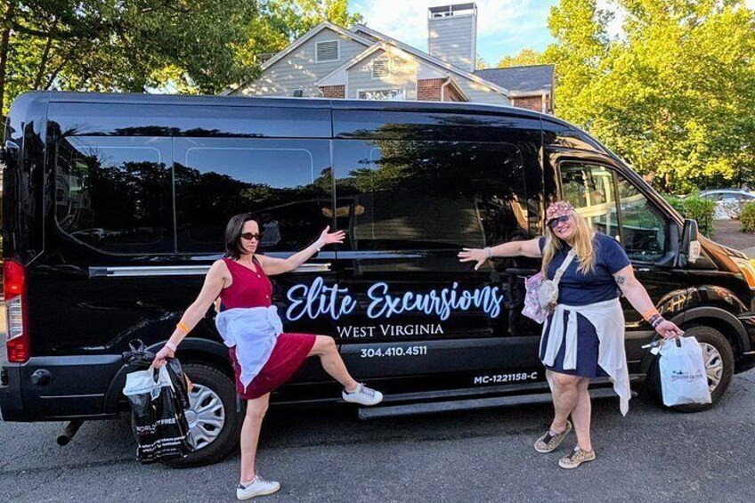 Two people standing next to a black van with 'Elite Excursions West Virginia' written on it. 2