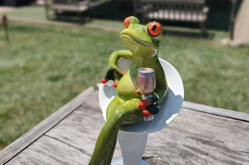 A frog figurine sitting on a white plate with a glass of wine. 3