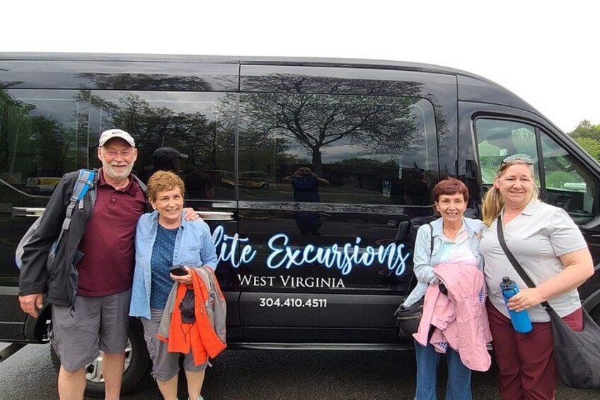 A group of people standing in front of a black van with 'Lite Excursions West Virginia' written on it. 4