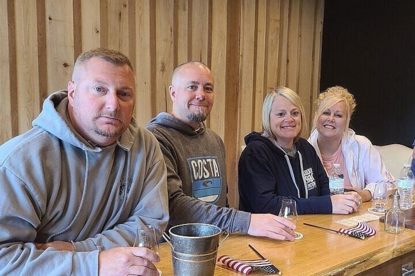 Four people seated at a wooden table with drinks and glasses. 4