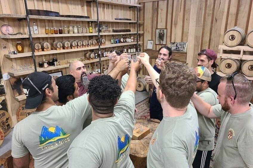 A group of people in a room with wooden shelves filled with bottles and barrels. 1