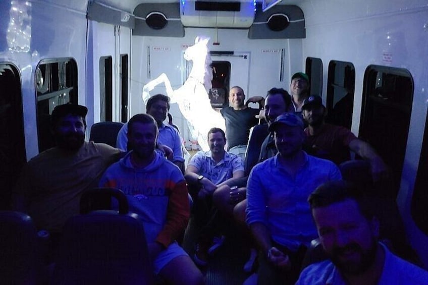 A group of people seated inside a vehicle with a large, illuminated sculpture of a horse in the background. 2