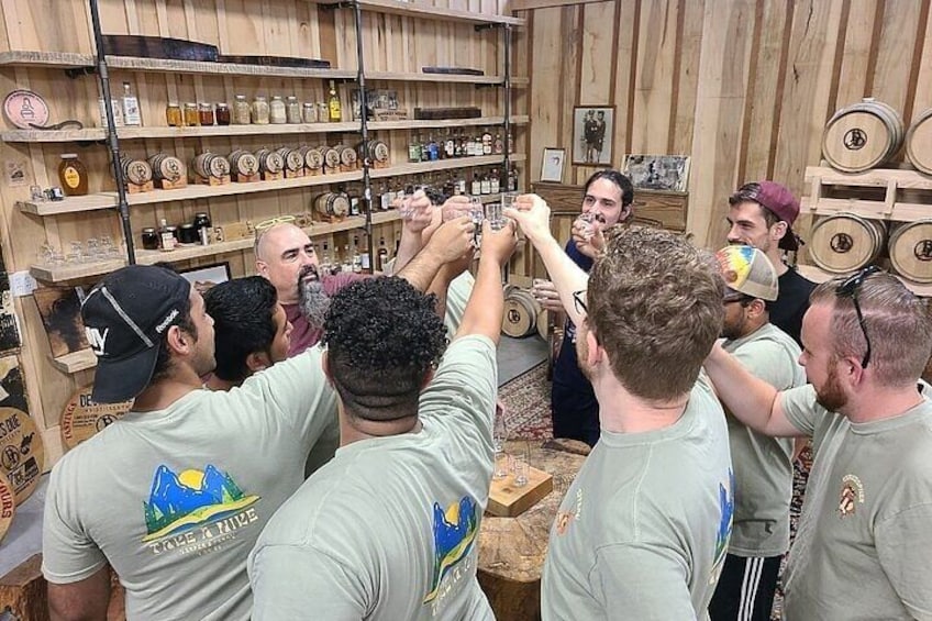 A group of people in a room with wooden shelves filled with bottles and barrels. 1