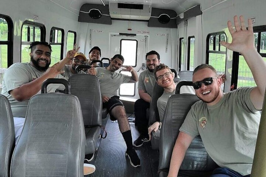 A group of people seated inside a bus, waving and smiling. 3