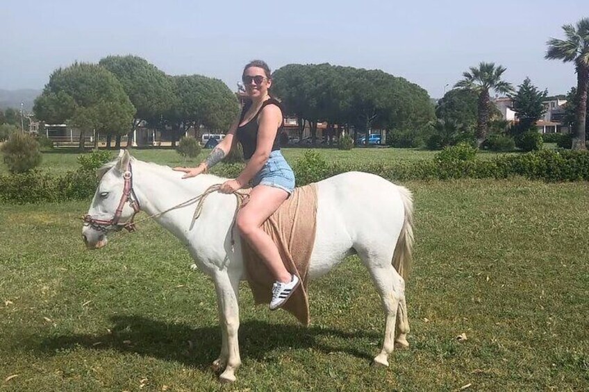 A person riding a white horse in a grassy field with trees and buildings in the background. 4