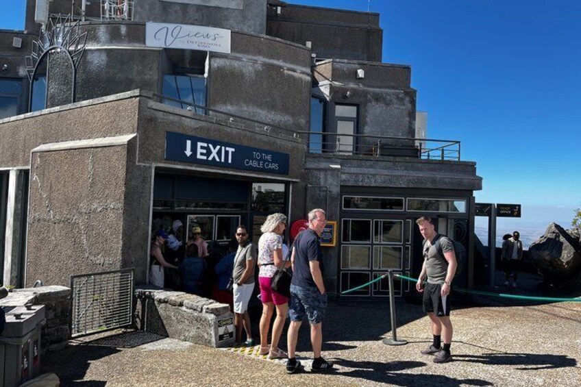 A building with an 'EXIT TO THE CABLE CARS' sign, a group of people near the entrance, and a clear sky. 2