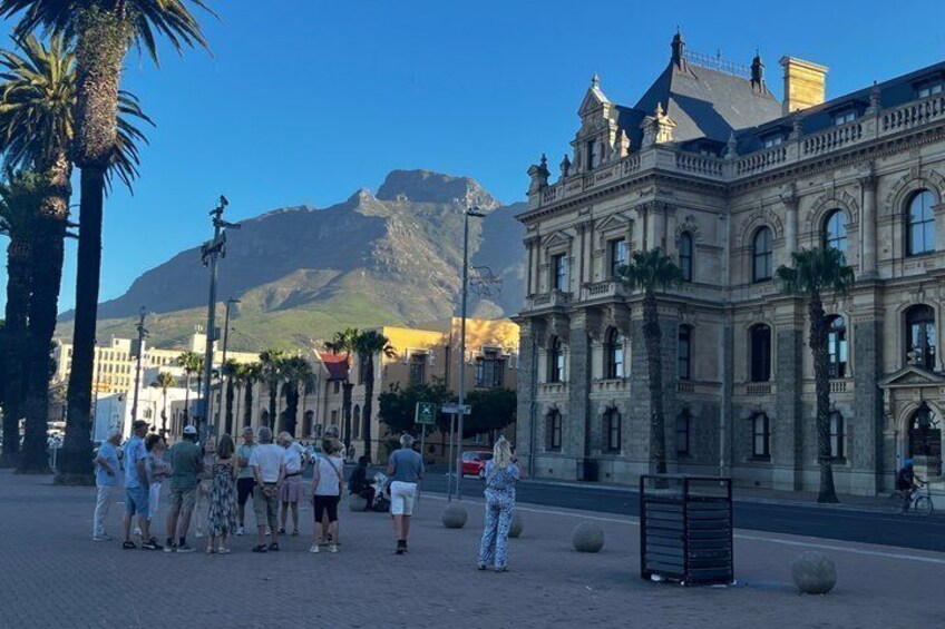 A group of people standing in a plaza with a historic building and a mountain in the background. 1