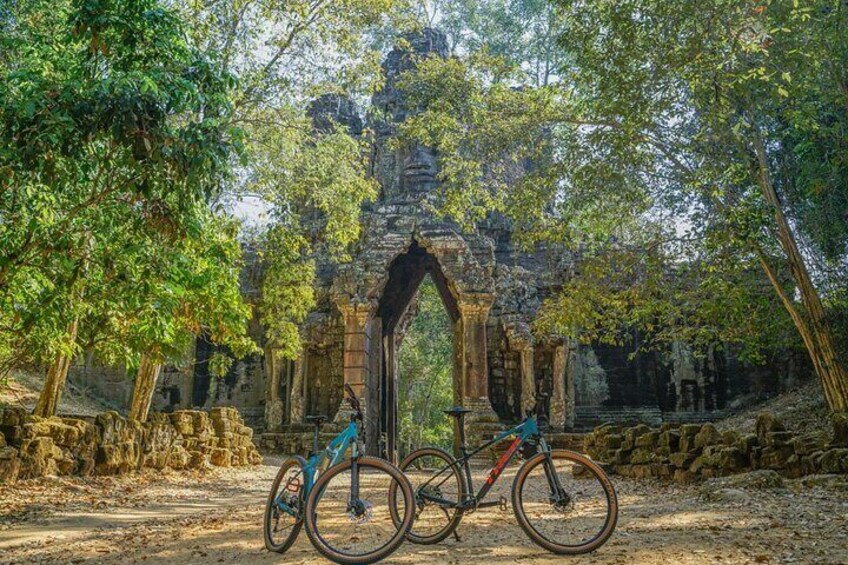 Un vélo est garé devant une arche en pierre ancienne, entourée d’arbres. 3