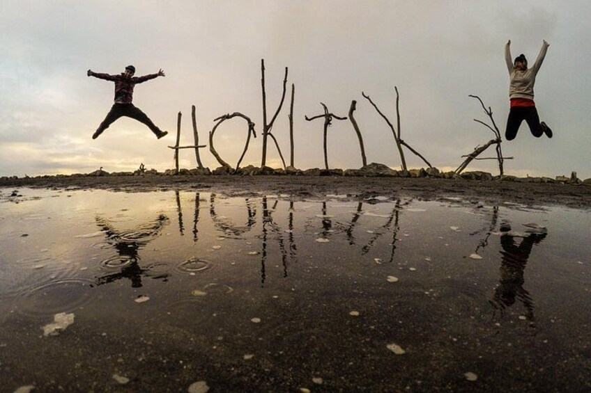 A person jumping in a puddle with reflections of trees and the word 'HOKKAIDO' written on the ground. 3