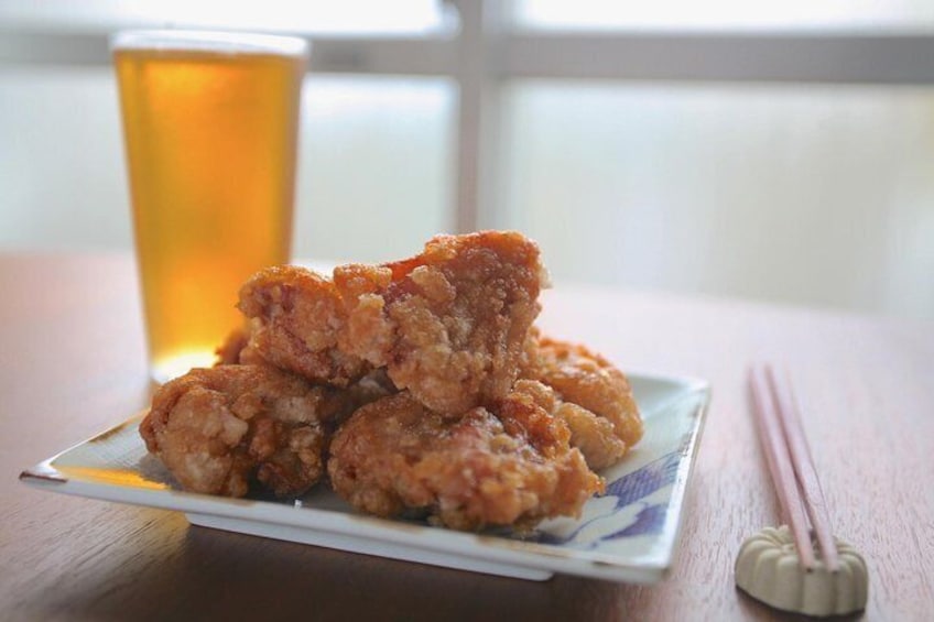Un plato de piezas de pollo frito sobre una mesa, con una jarra de cerveza y palillos. 3