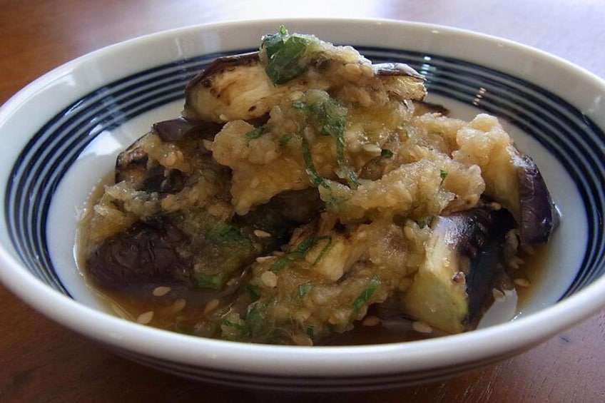Un tazón de comida con borde azul, que contiene una mezcla de verduras y posiblemente tofu, adornado con semillas de sésamo y hierbas picadas. 2