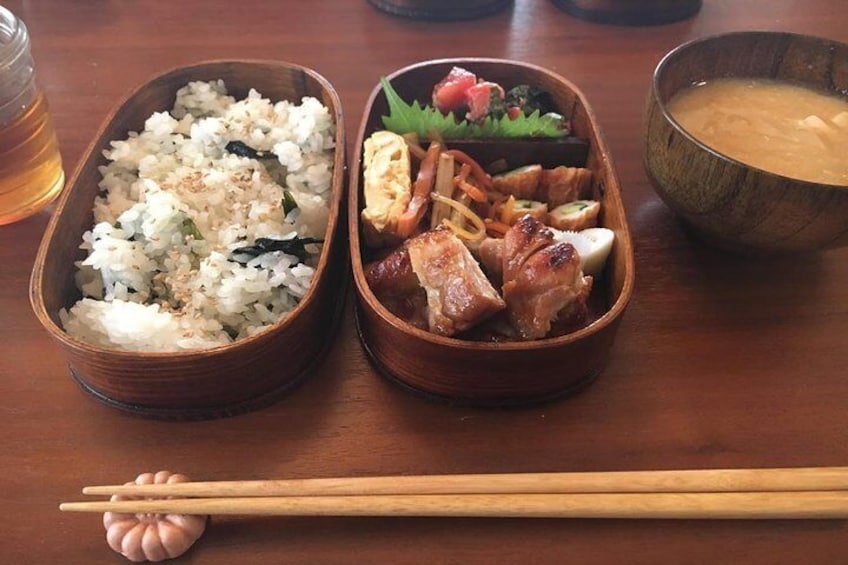 Una mesa de madera con dos bandejas de bento, una con arroz y la otra con carne y verduras, y un tazón de sopa. 5