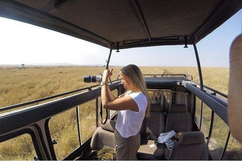A person holding a camera, seated in a vehicle with a view of a grassy landscape. 5