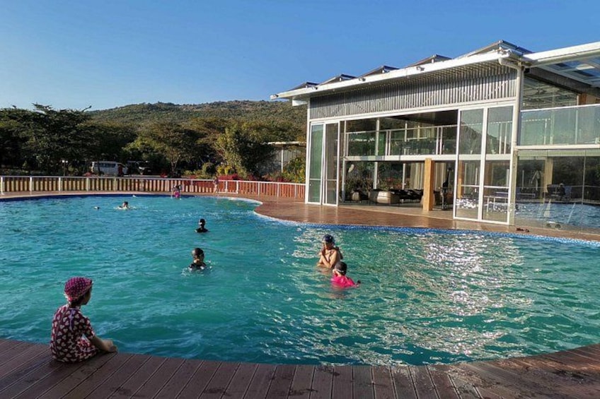 A swimming pool with people in the water, a wooden deck, and a modern building with large windows. 3