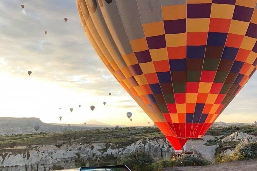 A hot air balloon with a colorful checkered pattern, set against a landscape of rocky terrain and distant hills. 2